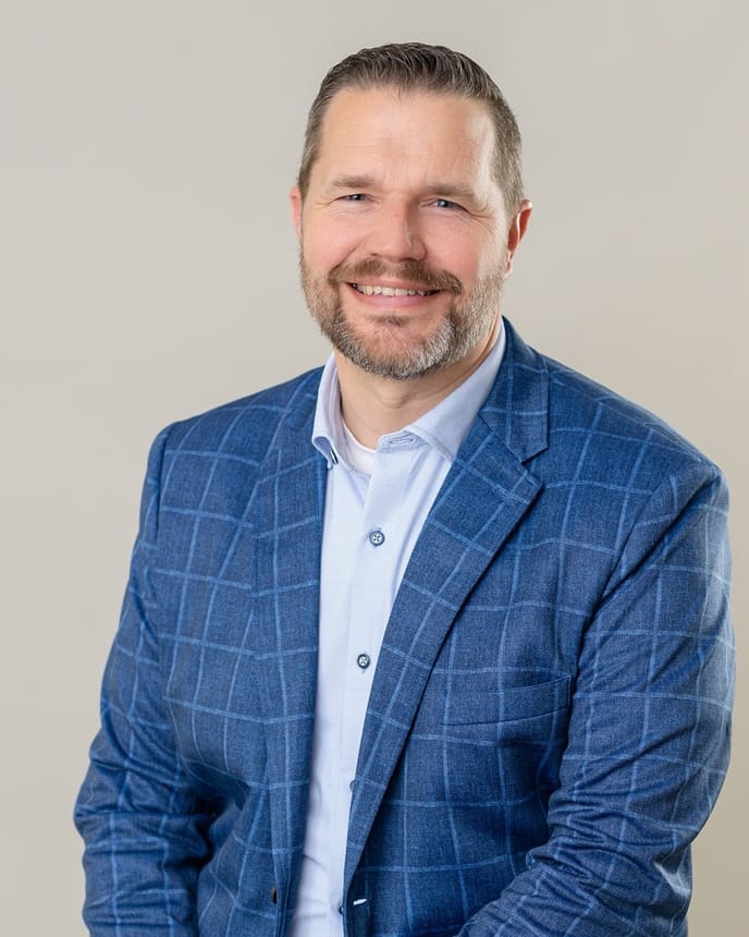 Chris Byers, wearing a blue blazer, photographed against a warm neutral backdrop.